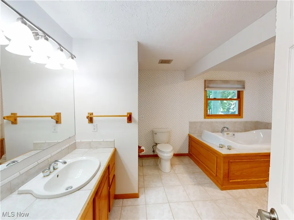 Full bath featuring a bath, vanity, light tile patterned floors, wallpapered walls, and a textured ceiling