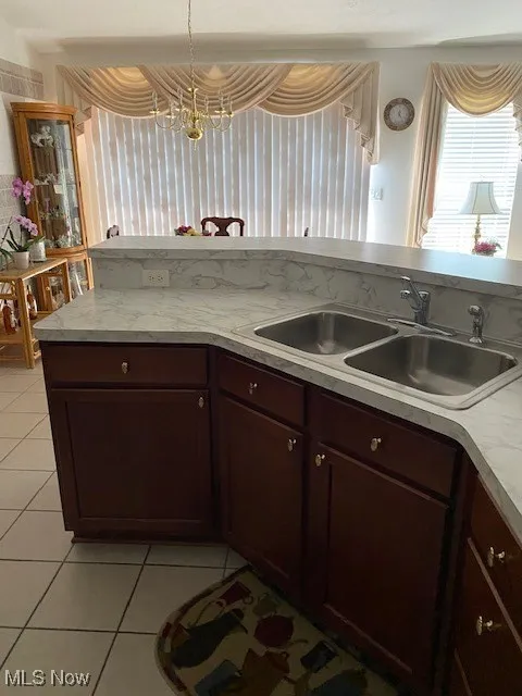 Kitchen with light tile patterned flooring, light countertops, a chandelier, and dark brown cabinetry