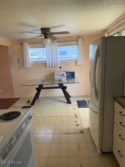 Kitchen featuring stove, refrigerator, light floors, white cabinetry, and healthy amount of natural light