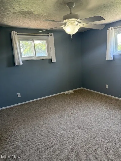 Empty room featuring carpet floors, a textured ceiling, and ceiling fan