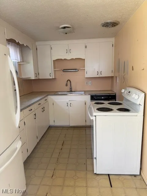 Kitchen with open shelves, light floors, stove, a textured ceiling, and refrigerator
