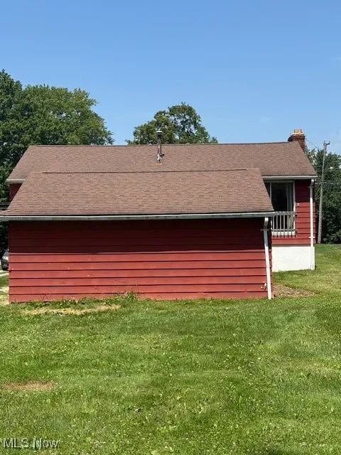 View of side of property featuring a chimney, a lawn, and roof with shingles
