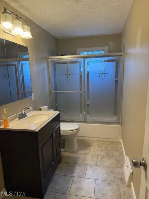 Bathroom featuring vanity, a textured ceiling, and combined bath / shower with glass door