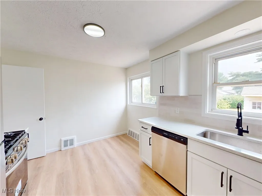 Kitchen with appliances with stainless steel finishes, light wood-style floors, decorative backsplash, light countertops, and a textured ceiling