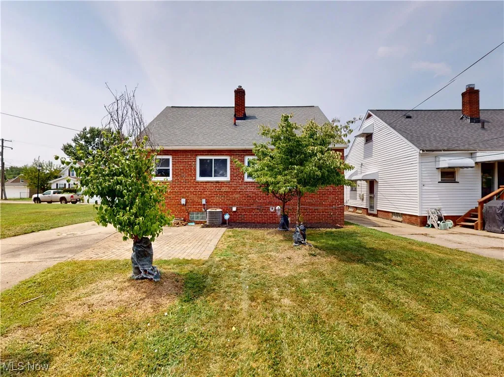 Back of property with a chimney, a yard, brick siding, and roof with shingles