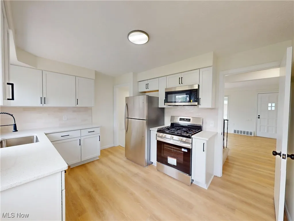 Kitchen with stainless steel appliances, white cabinets, light wood-style floors, decorative backsplash, and light stone countertops