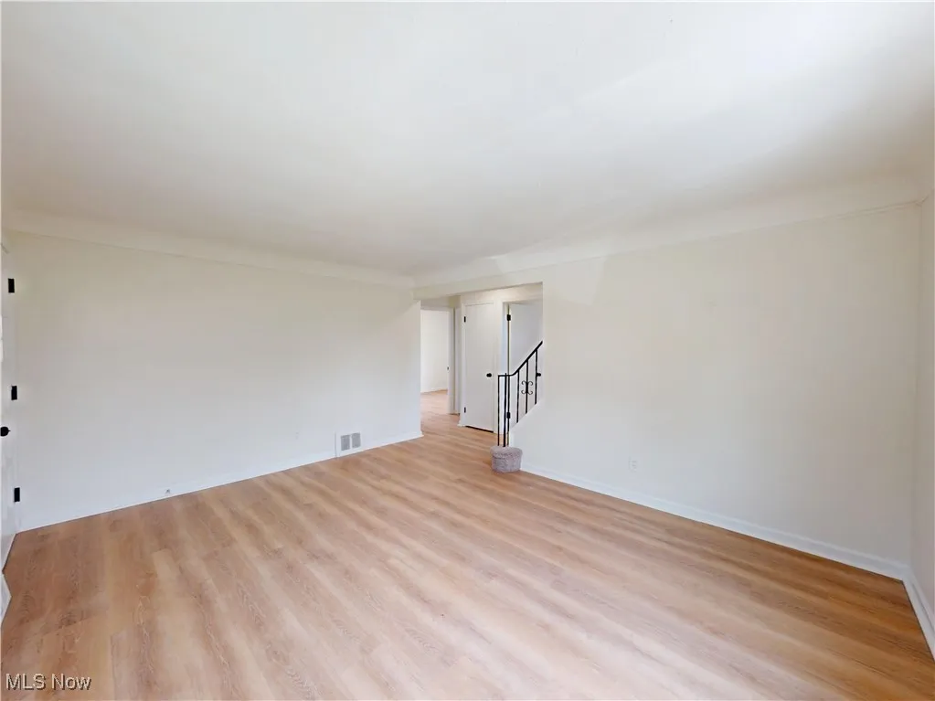 Empty room with light wood-type flooring, stairway, and crown molding
