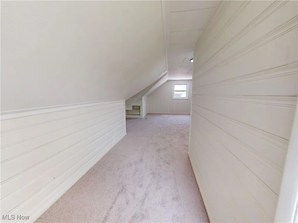 Additional living space with lofted ceiling, light colored carpet, and wood walls