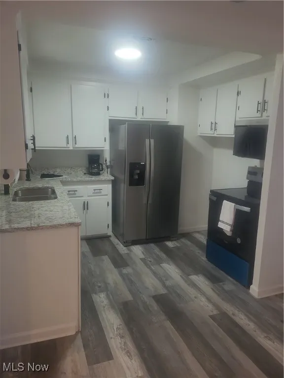 Kitchen with fridge with ice dispenser, stove, white cabinetry, light stone counters, and dark wood-style flooring