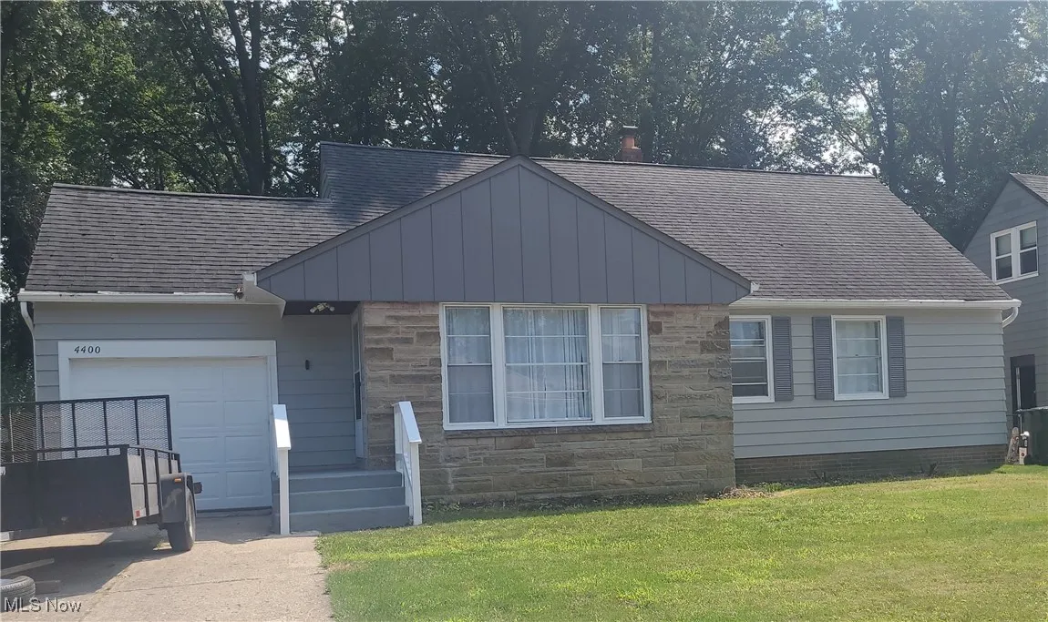 View of front of property with roof with shingles, stone siding, a front yard, and a garage