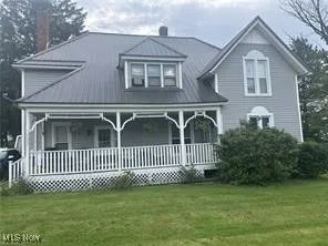 View of front of property with covered porch, a front yard, and a chimney