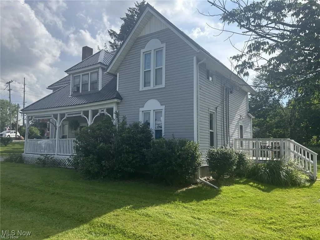 Back of house with a lawn, a chimney, covered porch, a wooden deck, and a metal roof