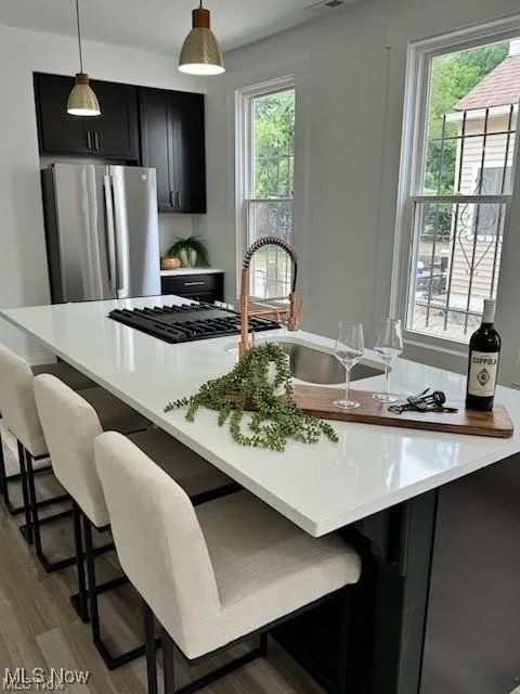 Kitchen with dark cabinets, freestanding refrigerator, a breakfast bar area, hanging light fixtures, and light countertops