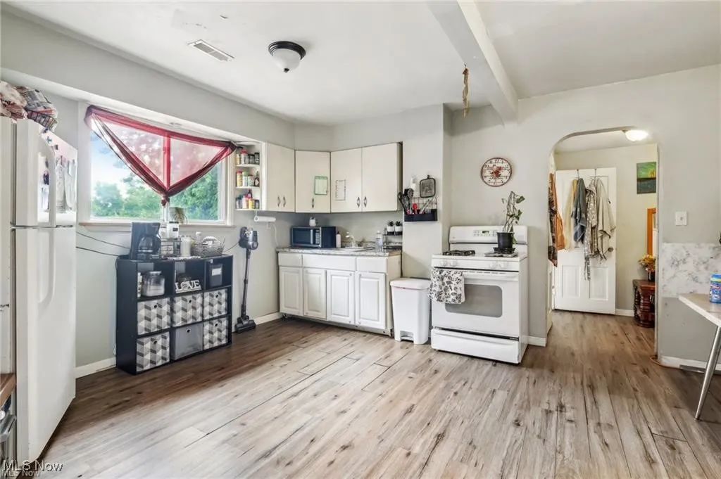 Kitchen with white appliances, white cabinetry, light countertops, light wood finished floors, and beam ceiling