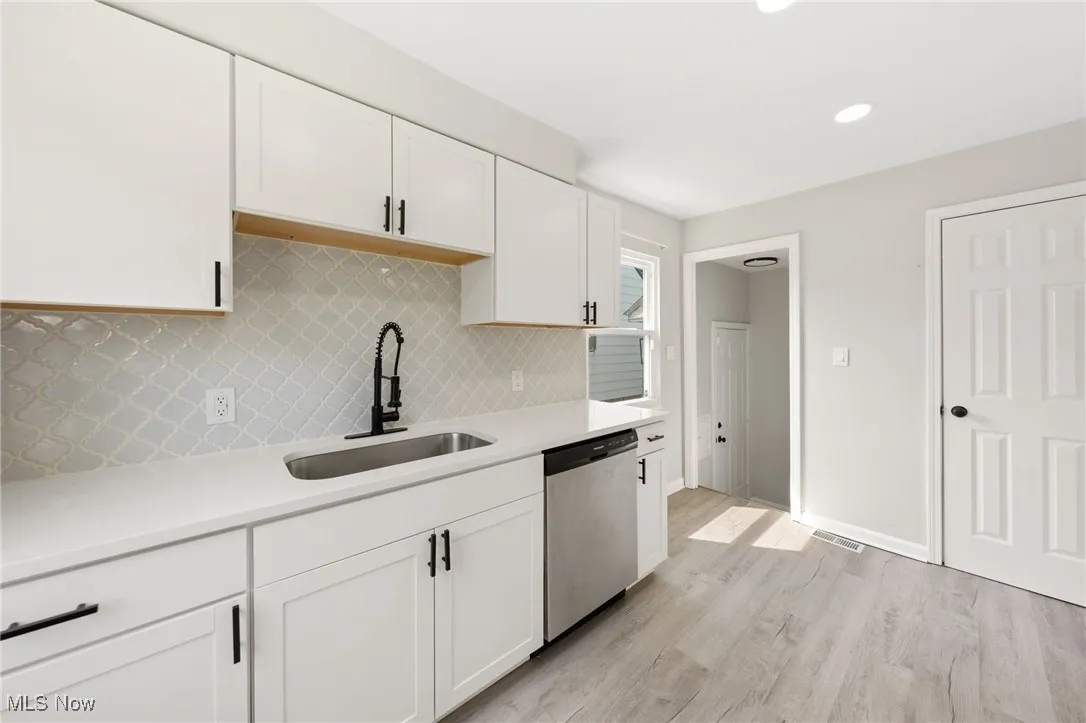 Kitchen featuring light countertops, stainless steel dishwasher, white cabinets, light wood-type flooring, and decorative backsplash