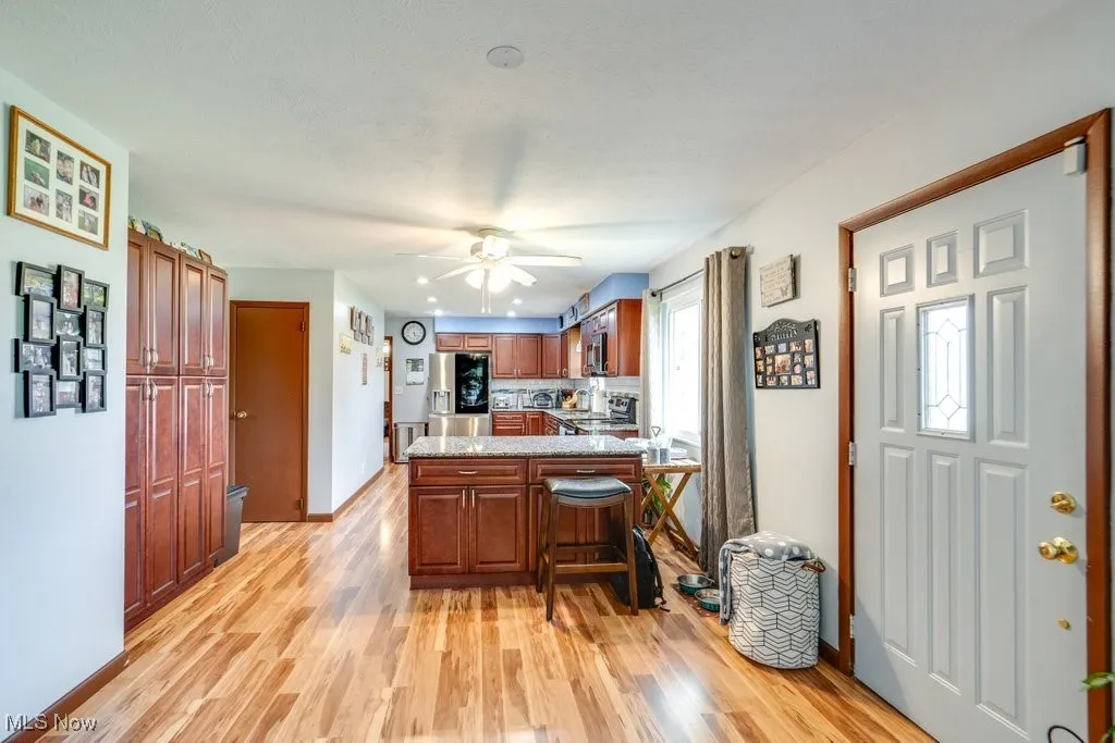 Kitchen with a peninsula, light wood-type flooring, appliances with stainless steel finishes, a breakfast bar, and a ceiling fan