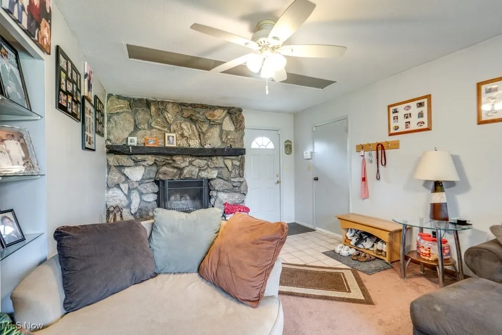 Carpeted living area with a stone fireplace and a ceiling fan