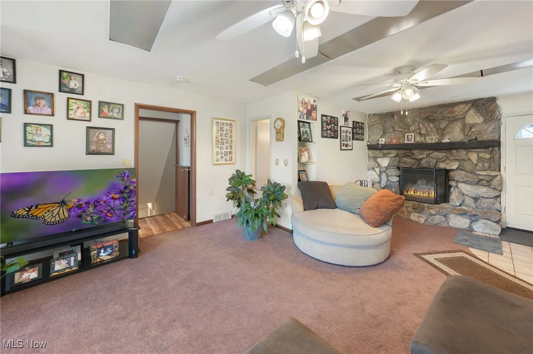 Living area featuring carpet, a fireplace, and a ceiling fan