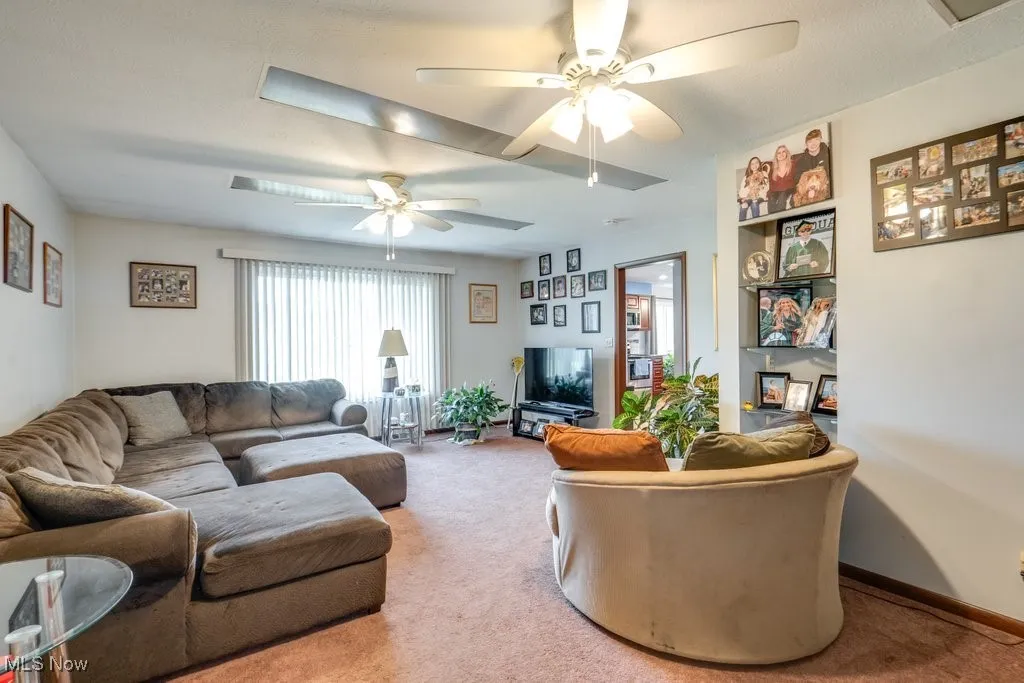 Carpeted living room with a ceiling fan and baseboards