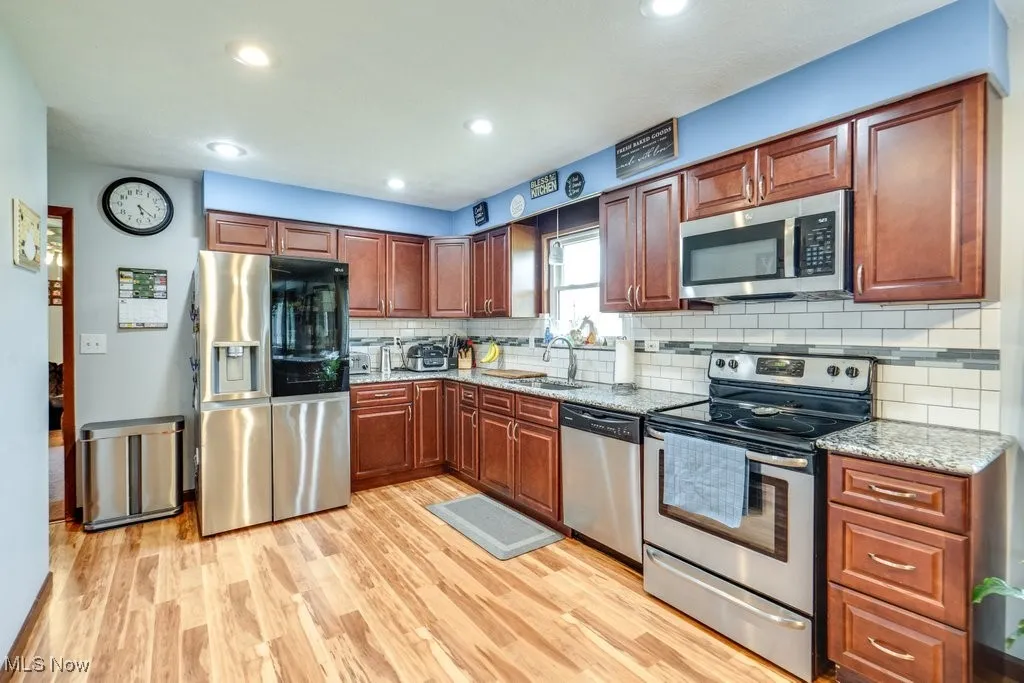 Kitchen with stainless steel appliances, tasteful backsplash, light wood-style floors, light stone counters, and recessed lighting