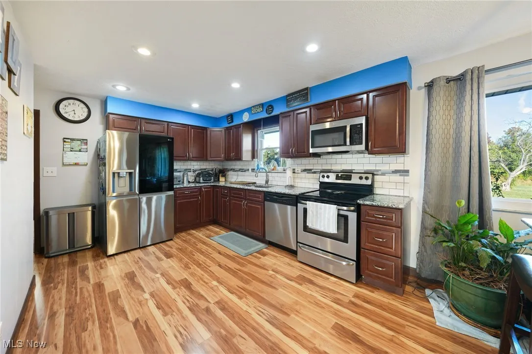 Kitchen with appliances with stainless steel finishes, light wood-type flooring, tasteful backsplash, dark brown cabinetry, and recessed lighting