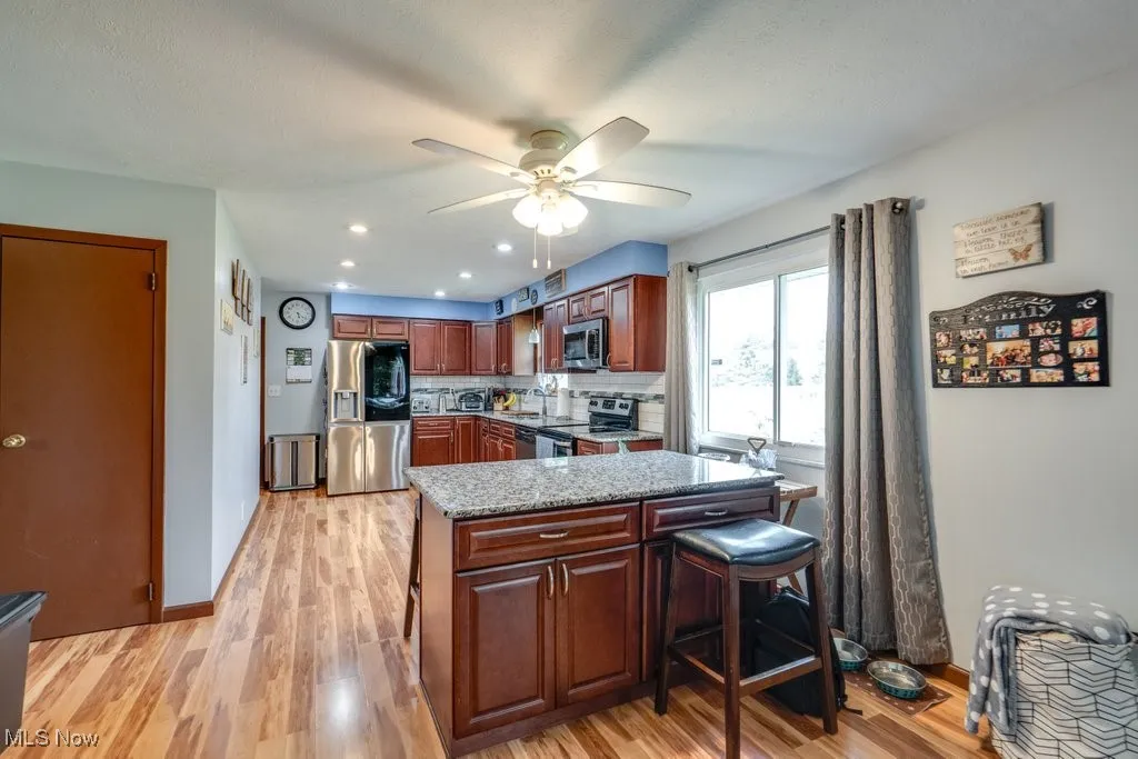Kitchen featuring appliances with stainless steel finishes, decorative backsplash, light wood-type flooring, light stone counters, and a ceiling fan