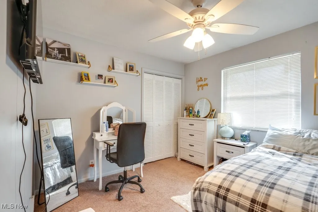 Bedroom with an office area, light carpet, a closet, and a ceiling fan