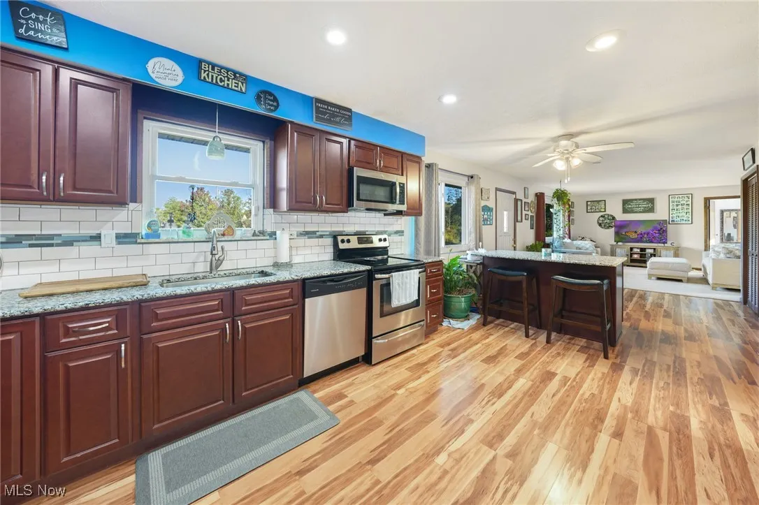 Kitchen featuring appliances with stainless steel finishes, light stone counters, a kitchen bar, open floor plan, and recessed lighting