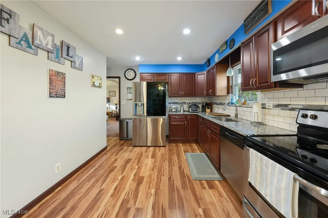 Kitchen featuring appliances with stainless steel finishes, light wood finished floors, backsplash, light stone countertops, and recessed lighting
