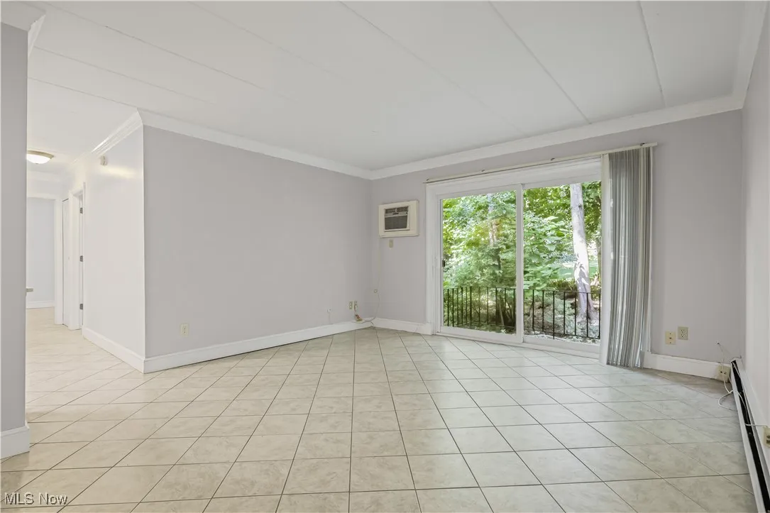 Unfurnished room featuring crown  molding, baseboard heating, light tile patterned floors, and a wall unit AC