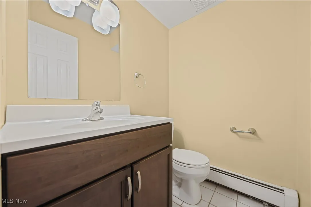 Half bathroom featuring a baseboard heating unit, vanity, and tile patterned flooring