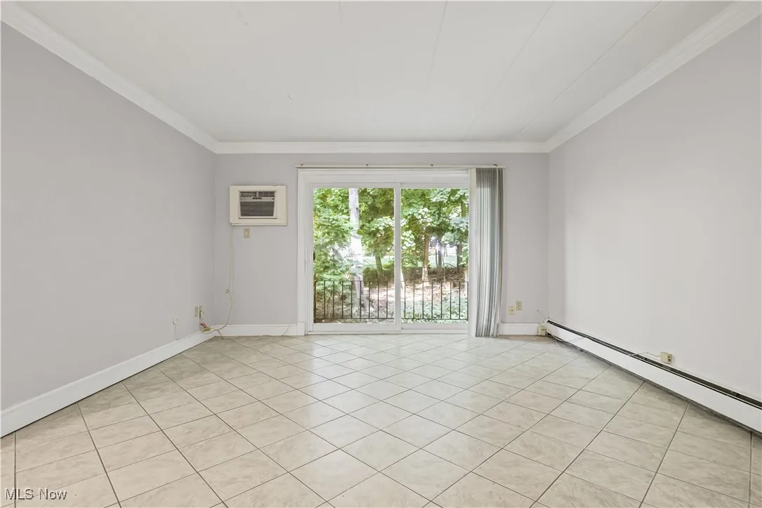 Unfurnished room with light tile patterned floors, ornamental molding, baseboard heating, and a wall unit AC
