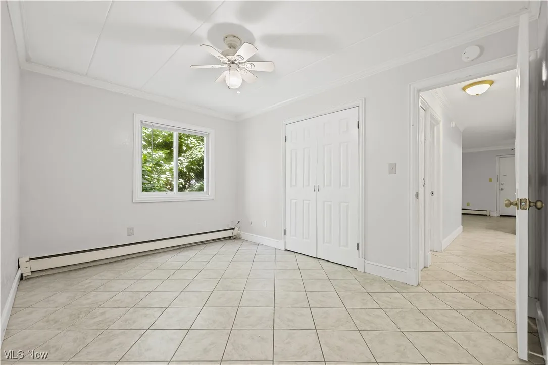 Unfurnished bedroom featuring crown molding, a baseboard heating unit, light tile patterned floors, a closet, and ceiling fan