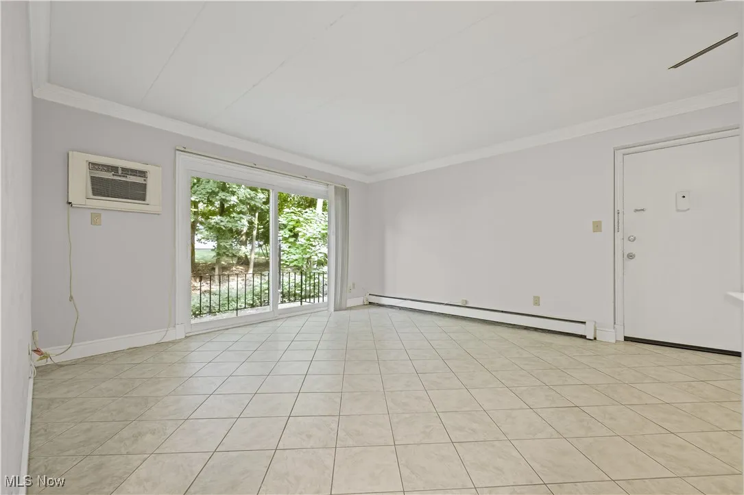 Empty room featuring crown molding, a baseboard heating unit, light tile patterned floors, and a wall unit AC
