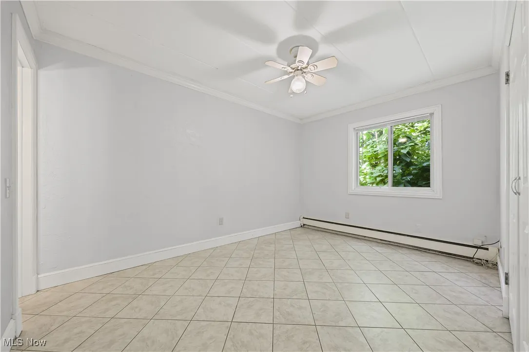 Empty room with crownl molding, baseboard heating, ceiling fan, and light tile patterned flooring