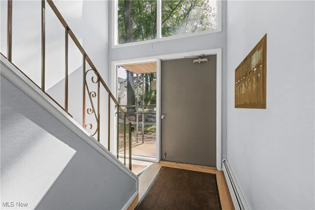 Foyer with baseboard heating, stairs, and tile patterned flooring
