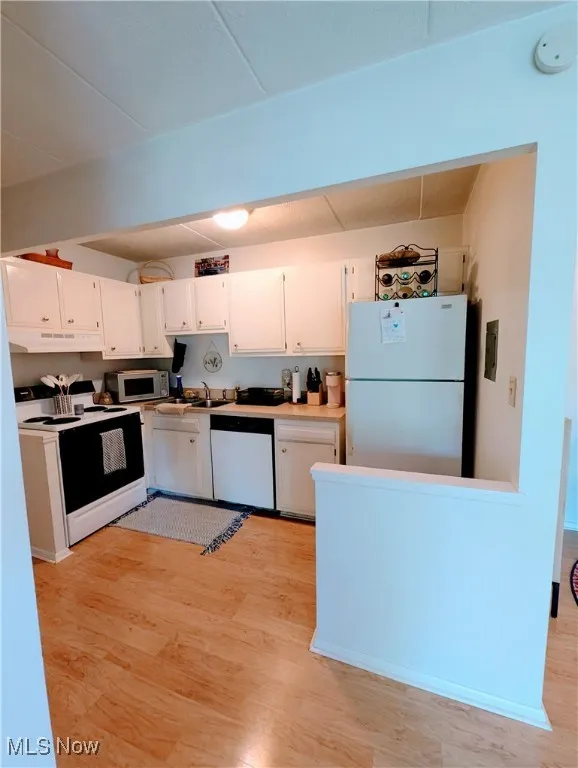 Kitchen featuring white appliances, white cabinets, laminate floors, and under cabinet range hood