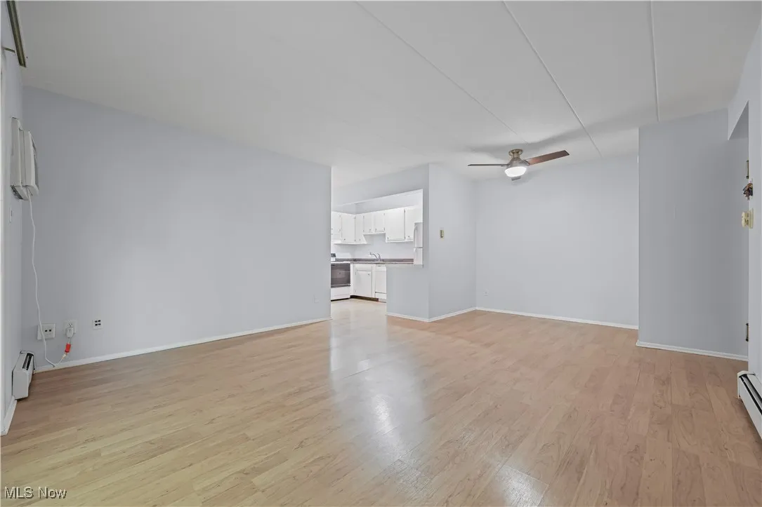 Unfurnished living room featuring laminate flooring, ceiling fan, a baseboard heating unit, and baseboard heating