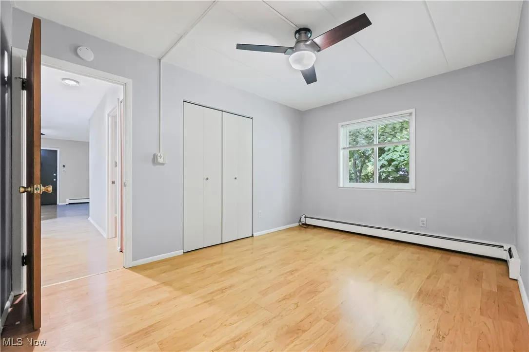 Unfurnished bedroom with light wood-style flooring, a baseboard heating unit, a closet, and ceiling fan