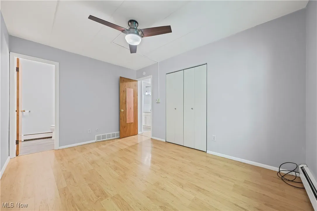 Unfurnished bedroom featuring wood finished floors, baseboard heating, connected bathroom, and a closet