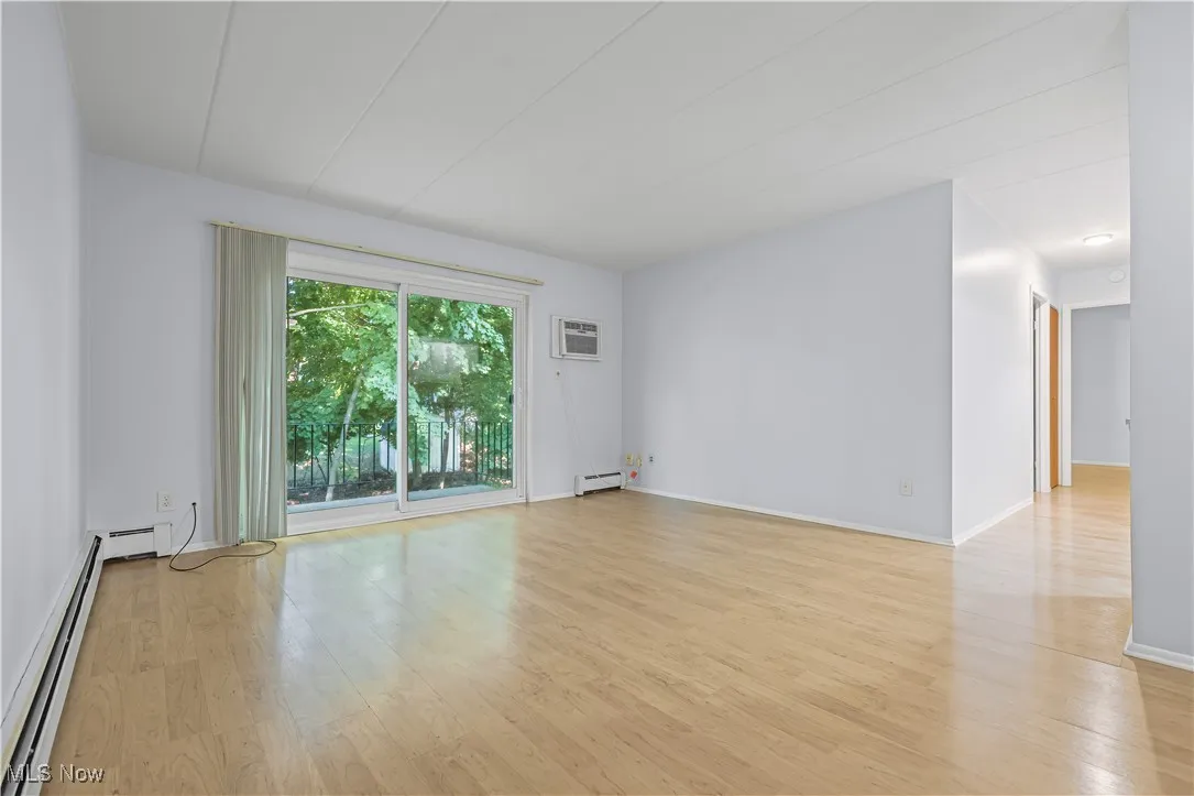 Empty room featuring light laminate flooring, baseboard heating, a baseboard heating unit, and a wall mounted air conditioner