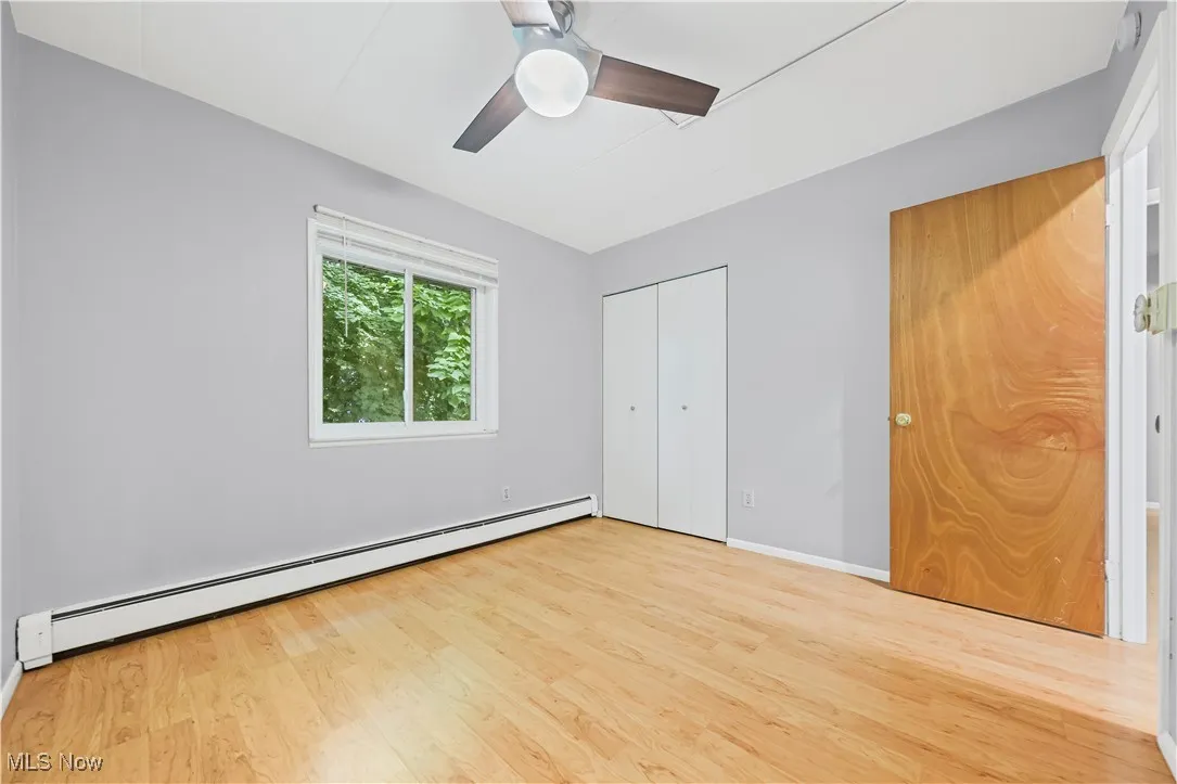 Unfurnished bedroom featuring a baseboard heating unit, wood finished floors, a closet, and ceiling fan