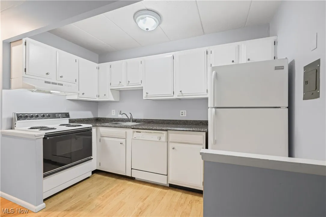 Kitchen featuring white appliances, dark countertops, range hood, light wood finished floors, and white cabinets
