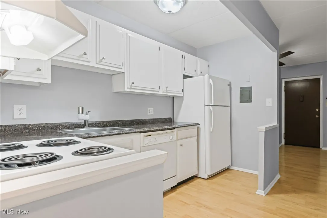 Kitchen with white cabinetry, laminate floors, dark countertops, and white appliances