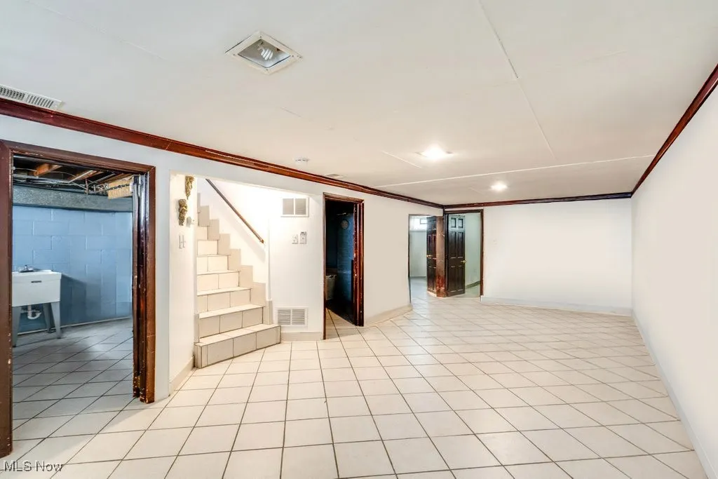 Finished below grade area with stairway, ornamental molding, light tile patterned flooring, and concrete block wall