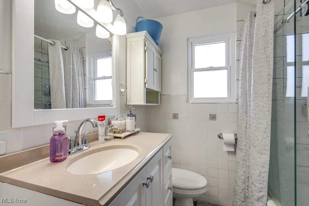 Bathroom featuring tile walls, vanity, tiled shower, and a wainscoted wall