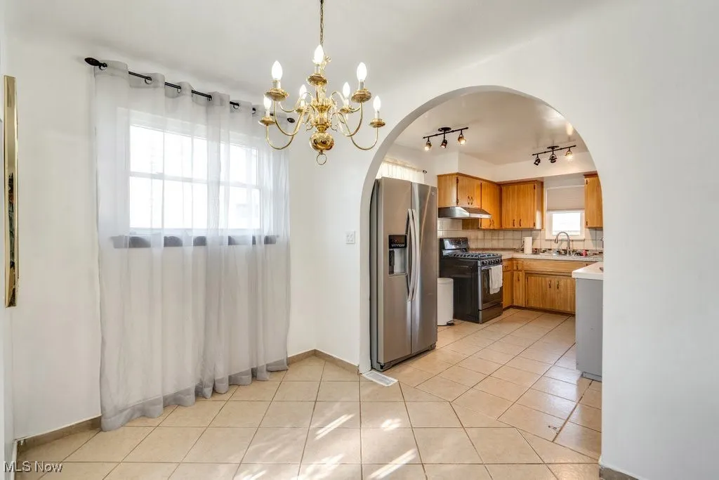 Kitchen featuring stainless steel fridge with ice dispenser, gas range, light countertops, light tile patterned floors, and arched walkways