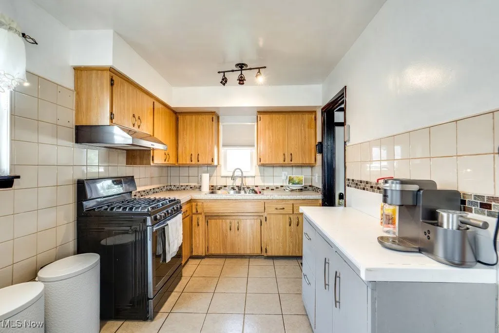 Kitchen with gas range, light tile patterned flooring, light countertops, under cabinet range hood, and backsplash