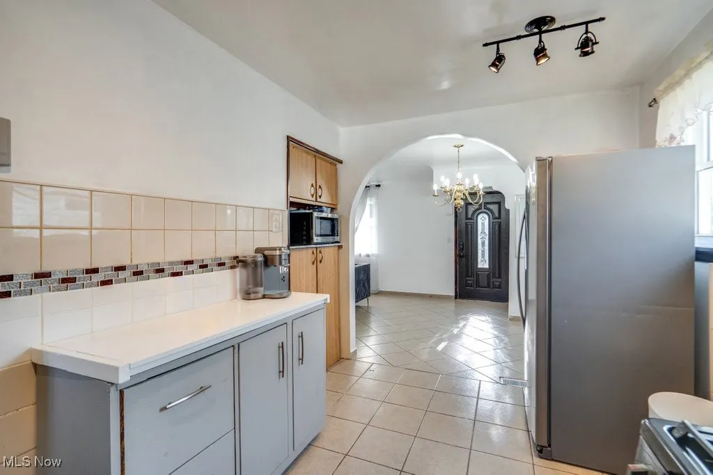 Kitchen with arched walkways, appliances with stainless steel finishes, light tile patterned floors, a chandelier, and gray cabinets
