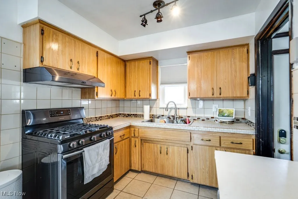 Kitchen featuring black gas stove, light countertops, under cabinet range hood, and tasteful backsplash